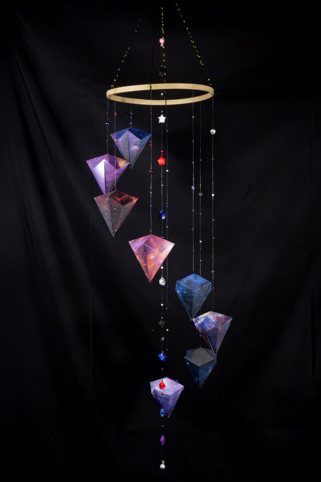 Mobile origami composé de diamants en papier et de perles, couleurs et motifs ambiance espace.