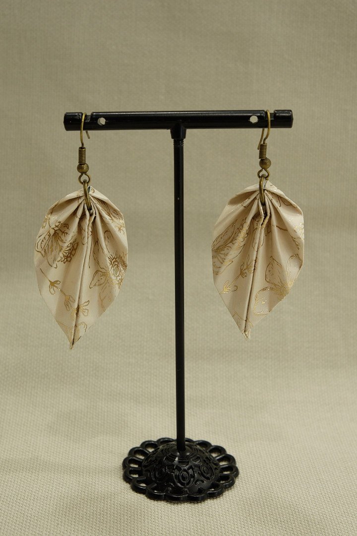 Boucle d'oreilles en origami en forme de feuille, de couleur beige avec des motifs couleur or